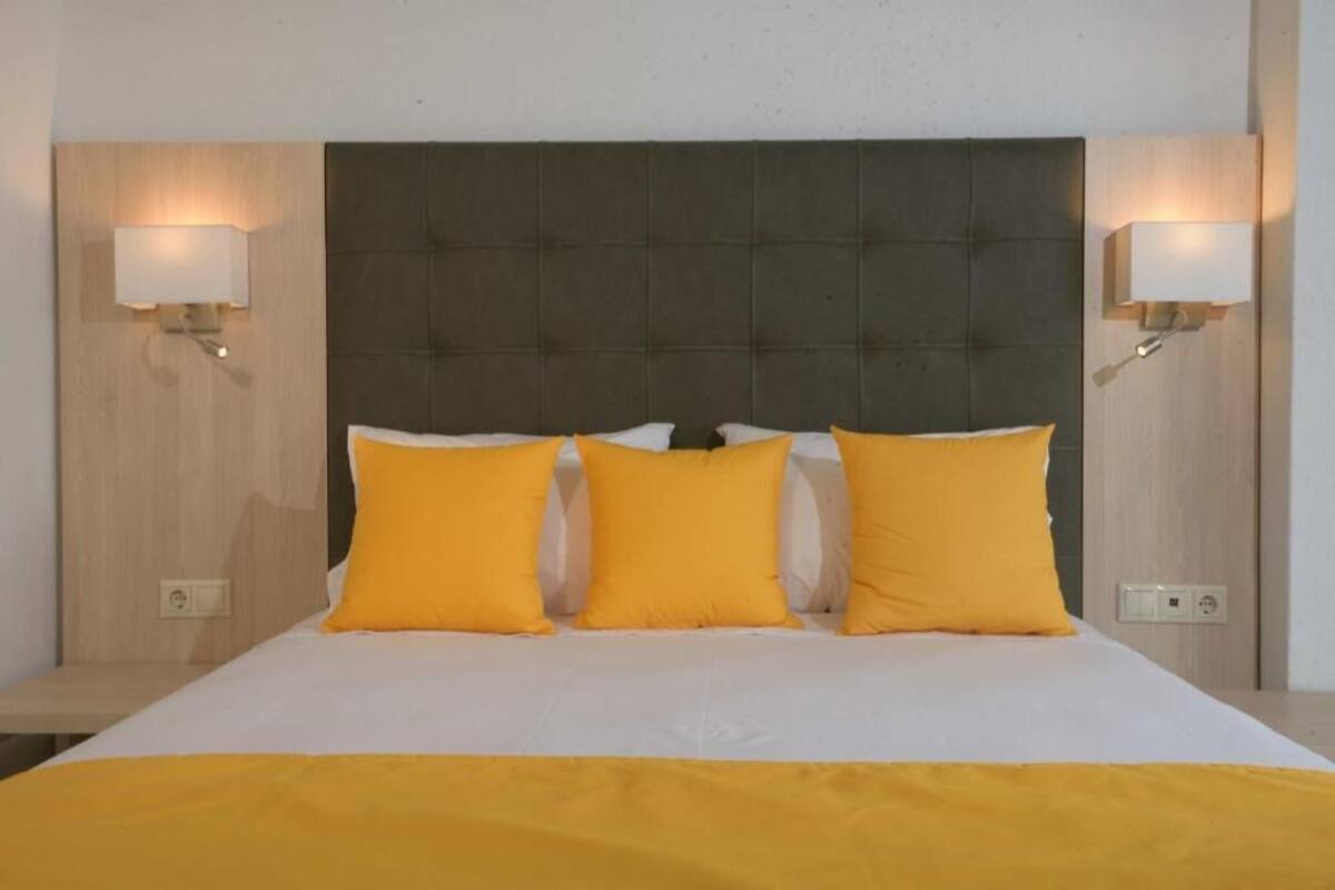 Een hotelkamer met een groot bed, drie gele kussens en twee wandlampen.