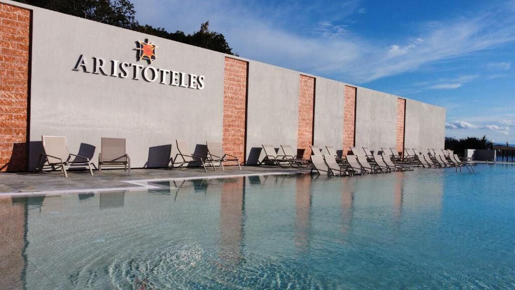 Un espace piscine avec des chaises longues et un bâtiment portant l’inscription « ARISTOTLE’S ».