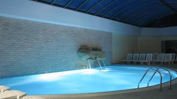 An indoor swimming pool with a brick wall, a rock feature, and lounge chairs.