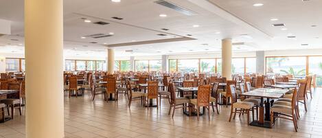 A spacious dining area with multiple tables and chairs, large pillars, and a high ceiling with recessed lighting.
