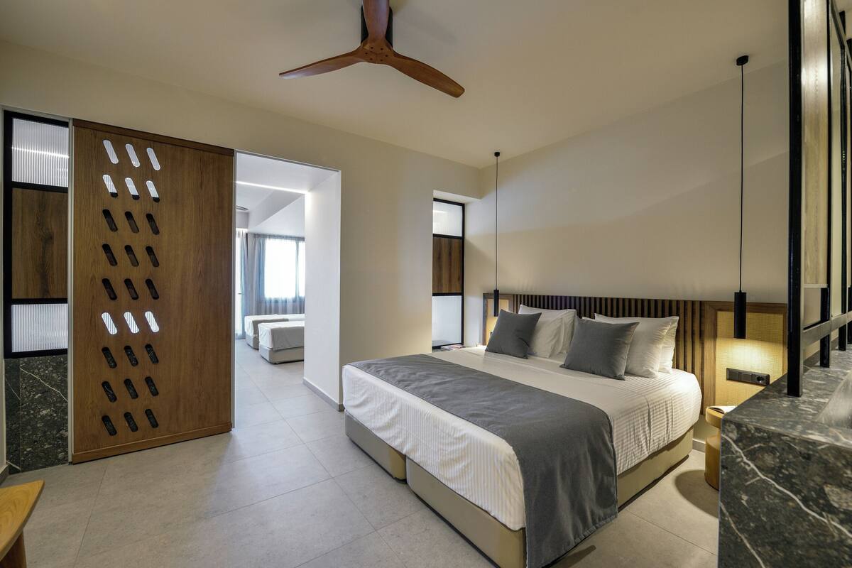 Een moderne slaapkamer met een groot bed, een houten scheidingswand met uitgesneden patronen, een plafondventilator en een marmeren accentmuur.