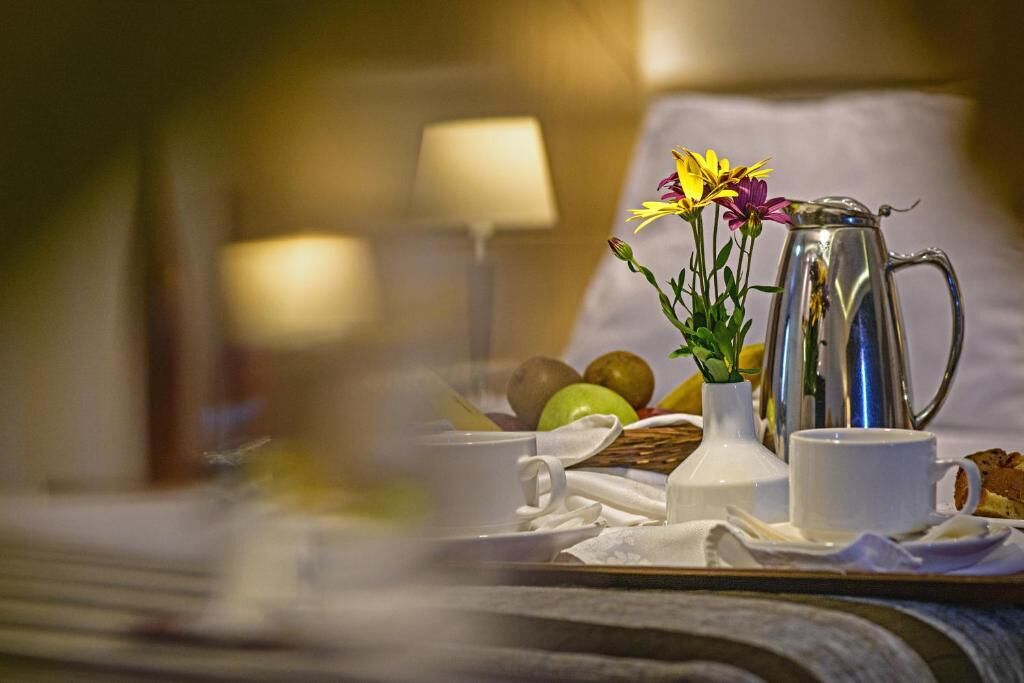 A breakfast tray with a coffee pot, cups, and fresh fruit on a bed.