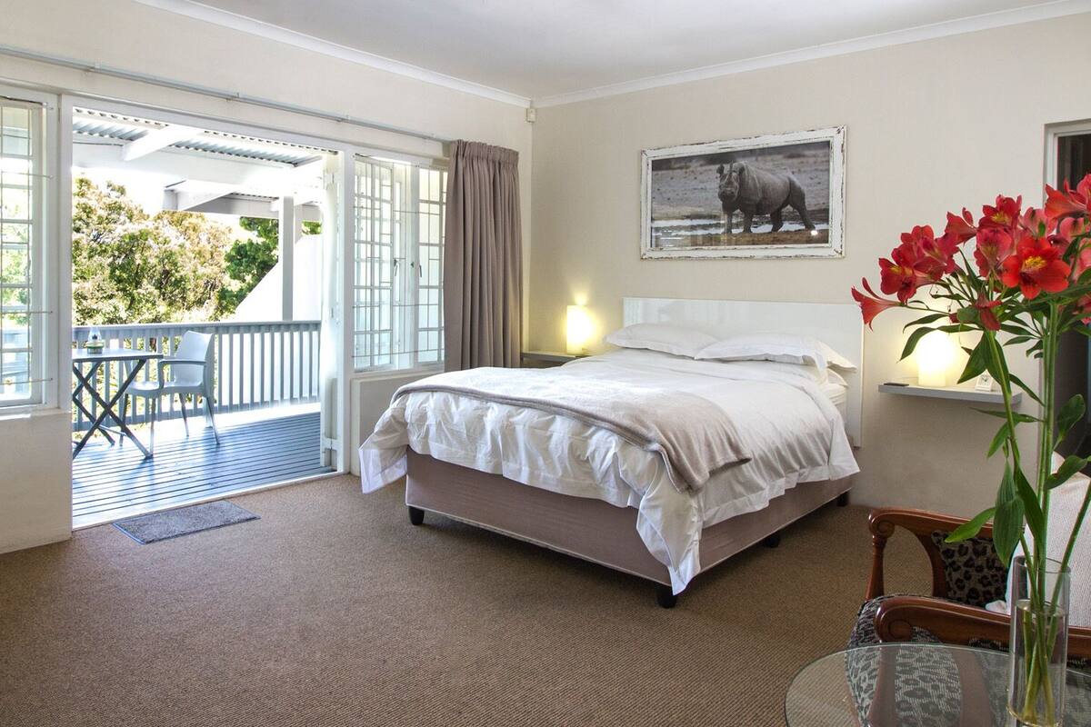 Ein Hotelzimmer mit Bett, Stuhl, Tisch und einem Balkon mit Blick auf Bäume.