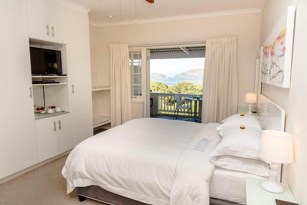 A bedroom with a bed, a TV, a desk, and a balcony with a view.