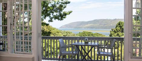 A balcony with a table and chairs, overlooking a scenic view of a lake and hills.