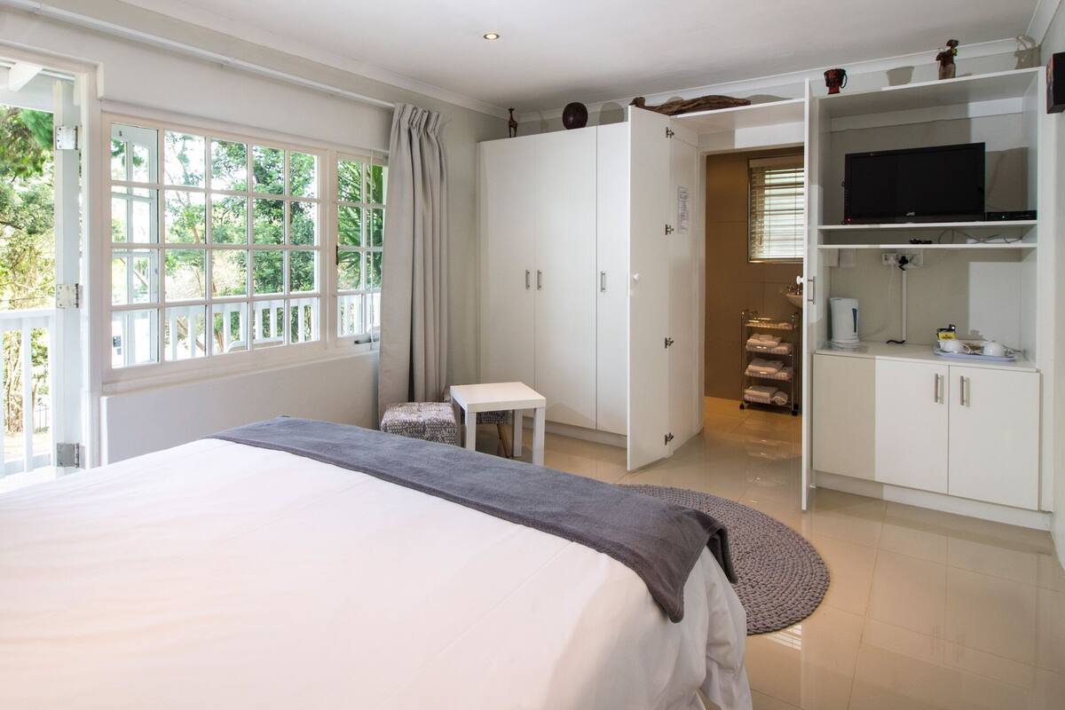 Ein Schlafzimmer mit einem großen Bett, einem Kleiderschrank, einem Fernseher und einem durch eine offene Tür einsehbaren Badezimmer.