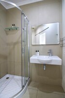 A modern bathroom with a glass shower enclosure, a white sink with a mirror above it, and a shelf with toiletries.
