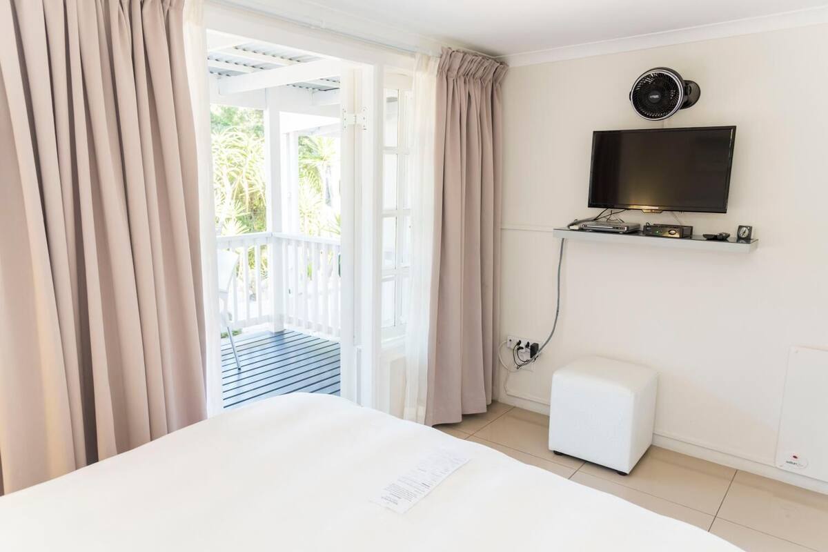 Ein Hotelzimmer mit Bett, Wandfernseher, kleinem Heizgerät und Blick auf Balkon.