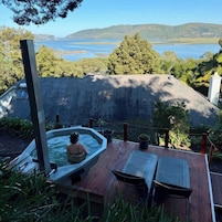 Un jacuzzi en una terraza de madera con vista a un lago y colinas.