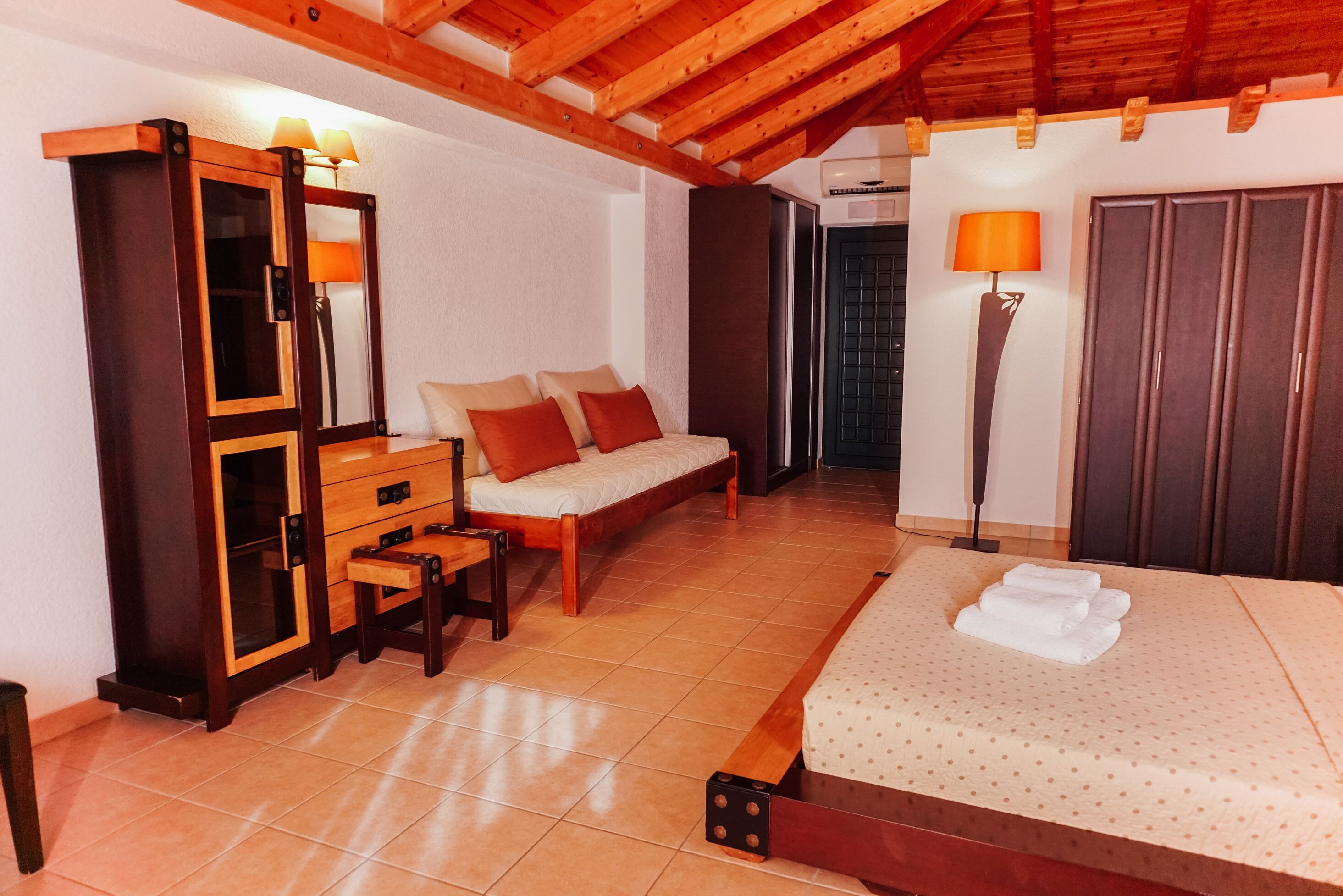 Un dormitorio con cama de madera, un sofá, un armario, un espejo y una lámpara de pie.