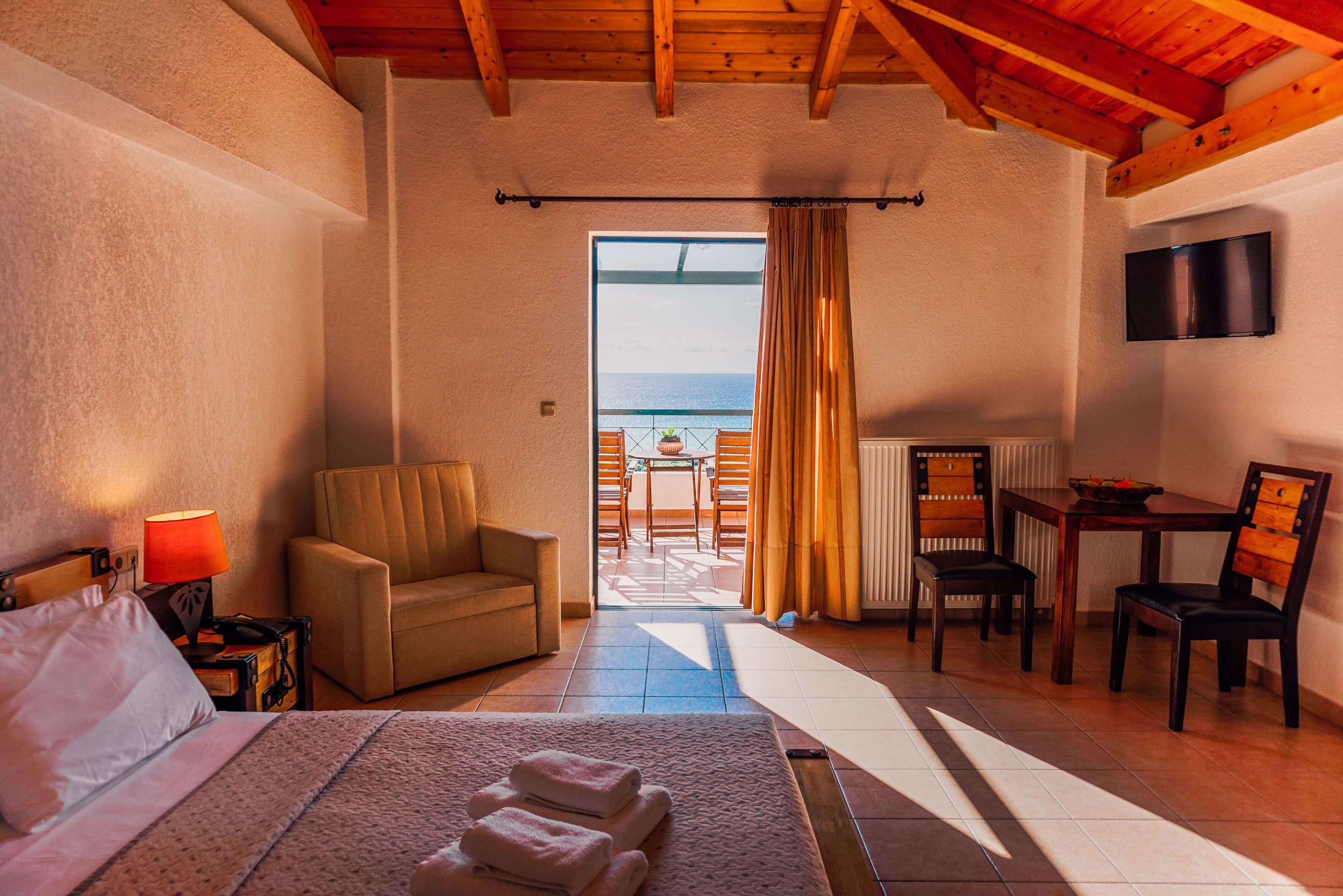 Ein Hotelzimmer mit Bett, Stuhl, Tisch und Meerblick durch ein großes Fenster.