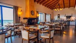 Un restaurante con mesas y sillas de madera, una chimenea y ventanas amplias con vistas panorámicas.