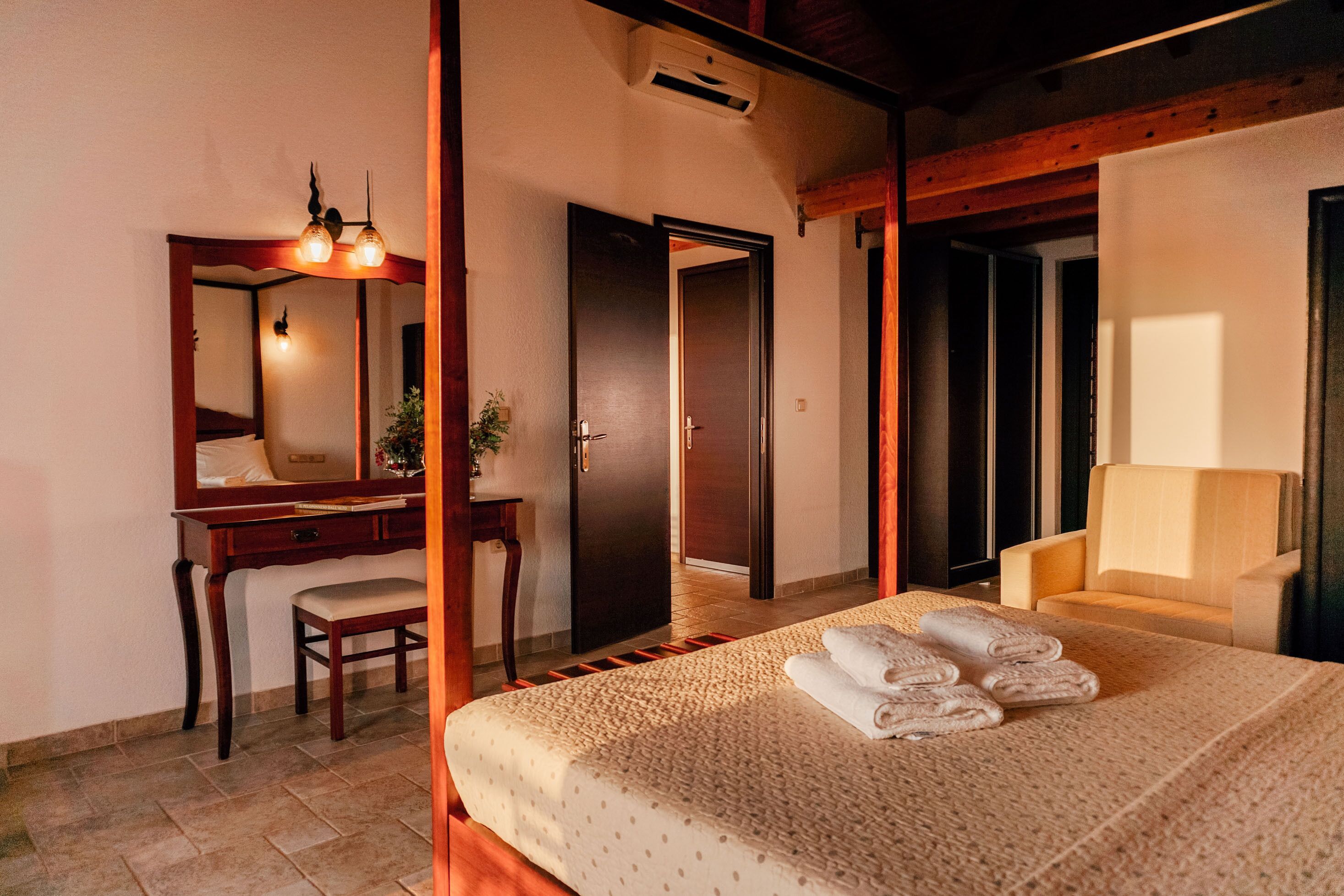 Une chambre d’hôtel comprenant un lit, un bureau, une chaise, un miroir et une porte donnant sur une autre pièce.