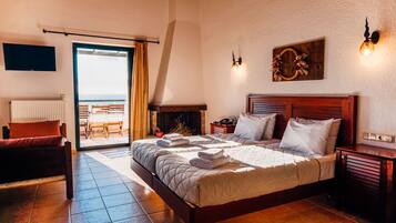 A bedroom with a large bed, a wooden headboard, a fireplace, a TV mounted on the wall, and a balcony with a view.