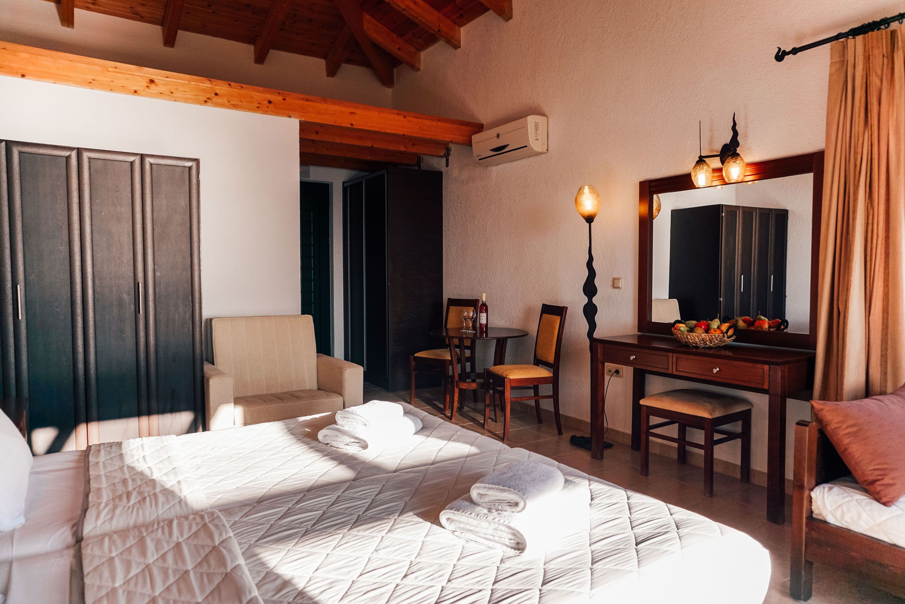 A hotel room with a bed, a desk, a chair, a small table, and a mirror.