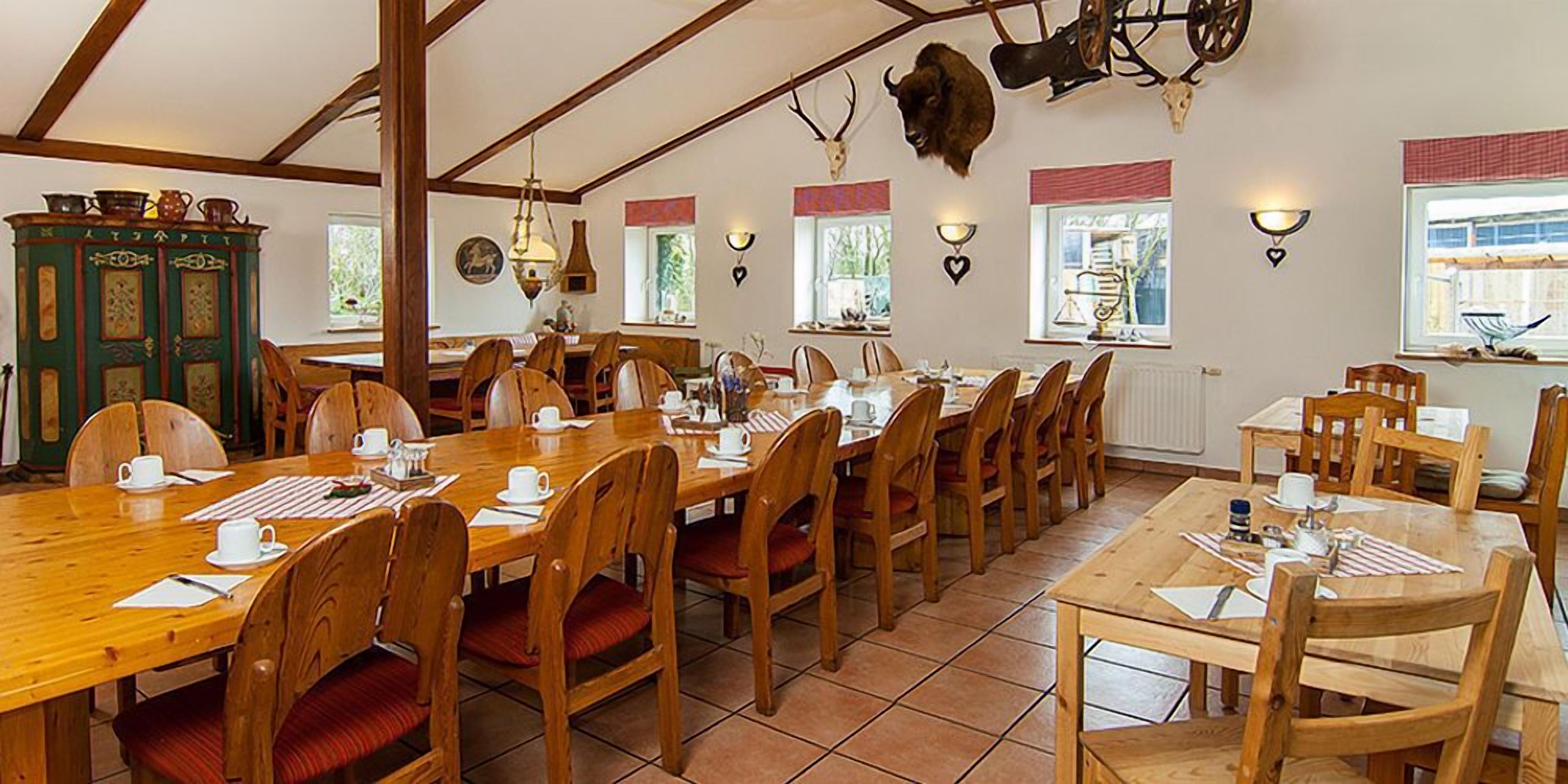 Un'area pranzo con tavoli e sedie in legno, un mobiletto verde con stoviglie e un grande corno di cervo appeso al muro.