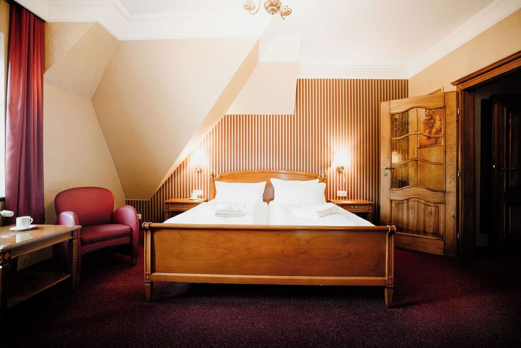 Una habitación de hotel con una cama de madera, una silla roja, un escritorio con una taza y un armario de madera.