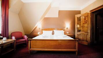 Una habitación de hotel con una cama de madera, una silla roja, un escritorio con una taza y un armario de madera.
