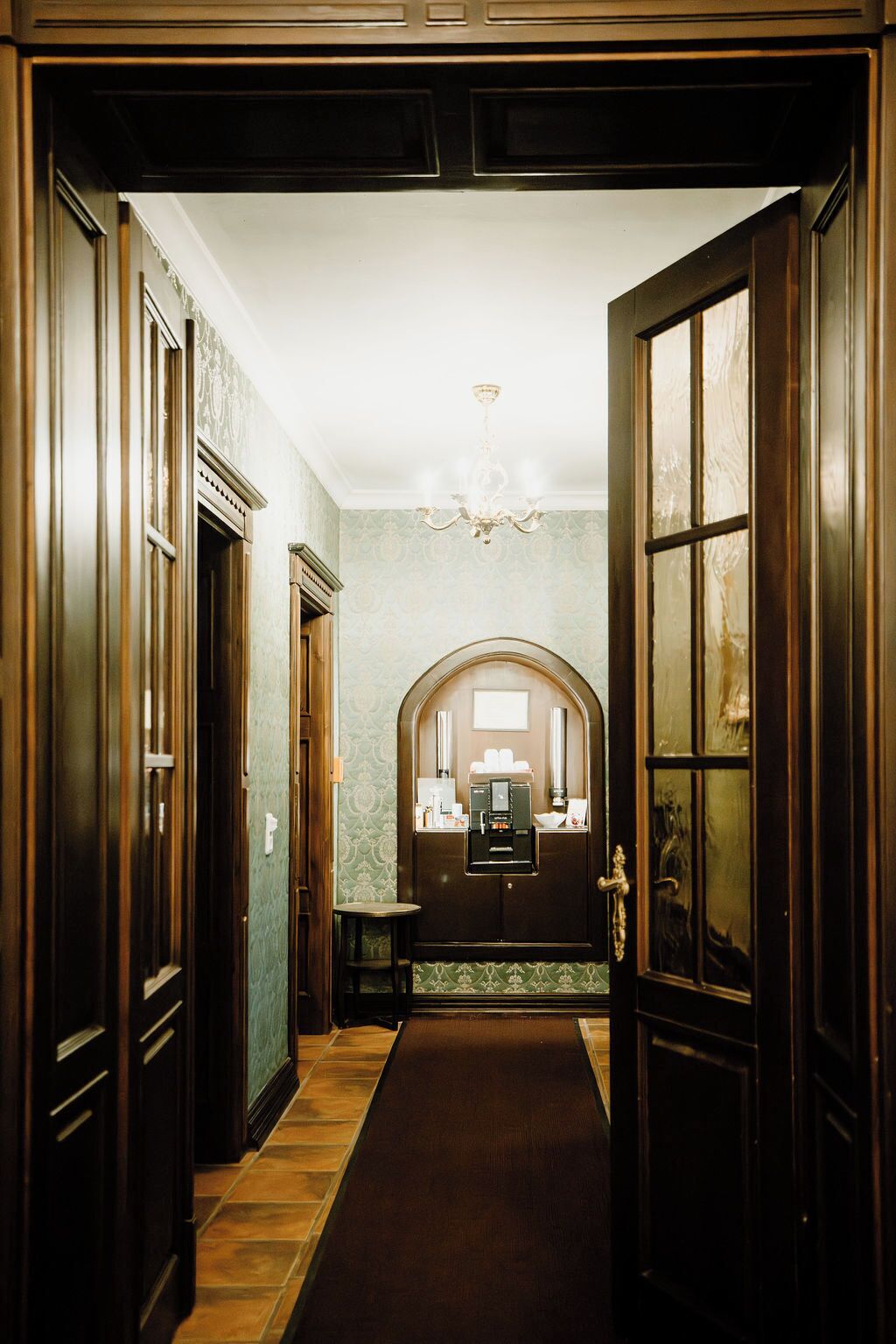 A hallway with a wooden door, a chandelier, and a coffee machine.