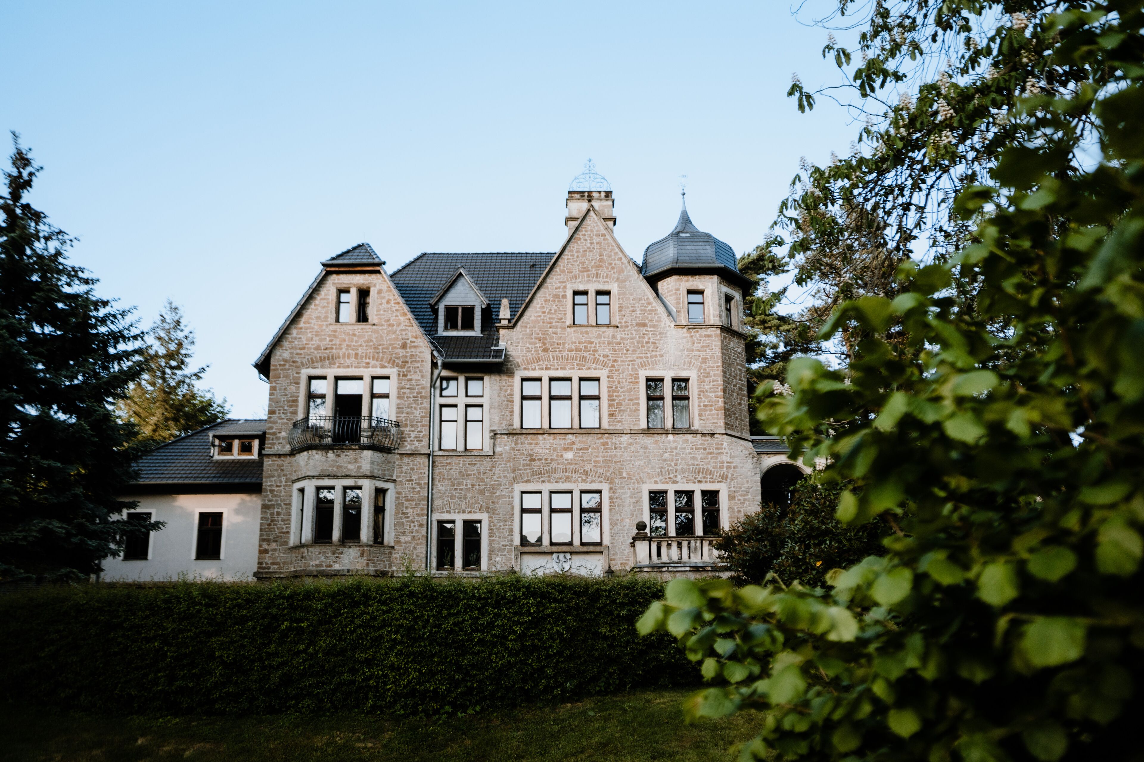 A large, multi-story stone building with a symmetrical facade, multiple windows, and a turret.