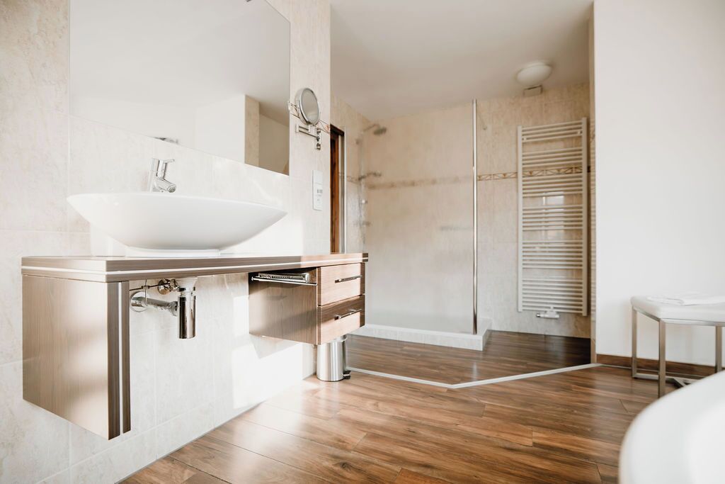 A modern bathroom with a large sink, a walk-in shower, and a towel rack.