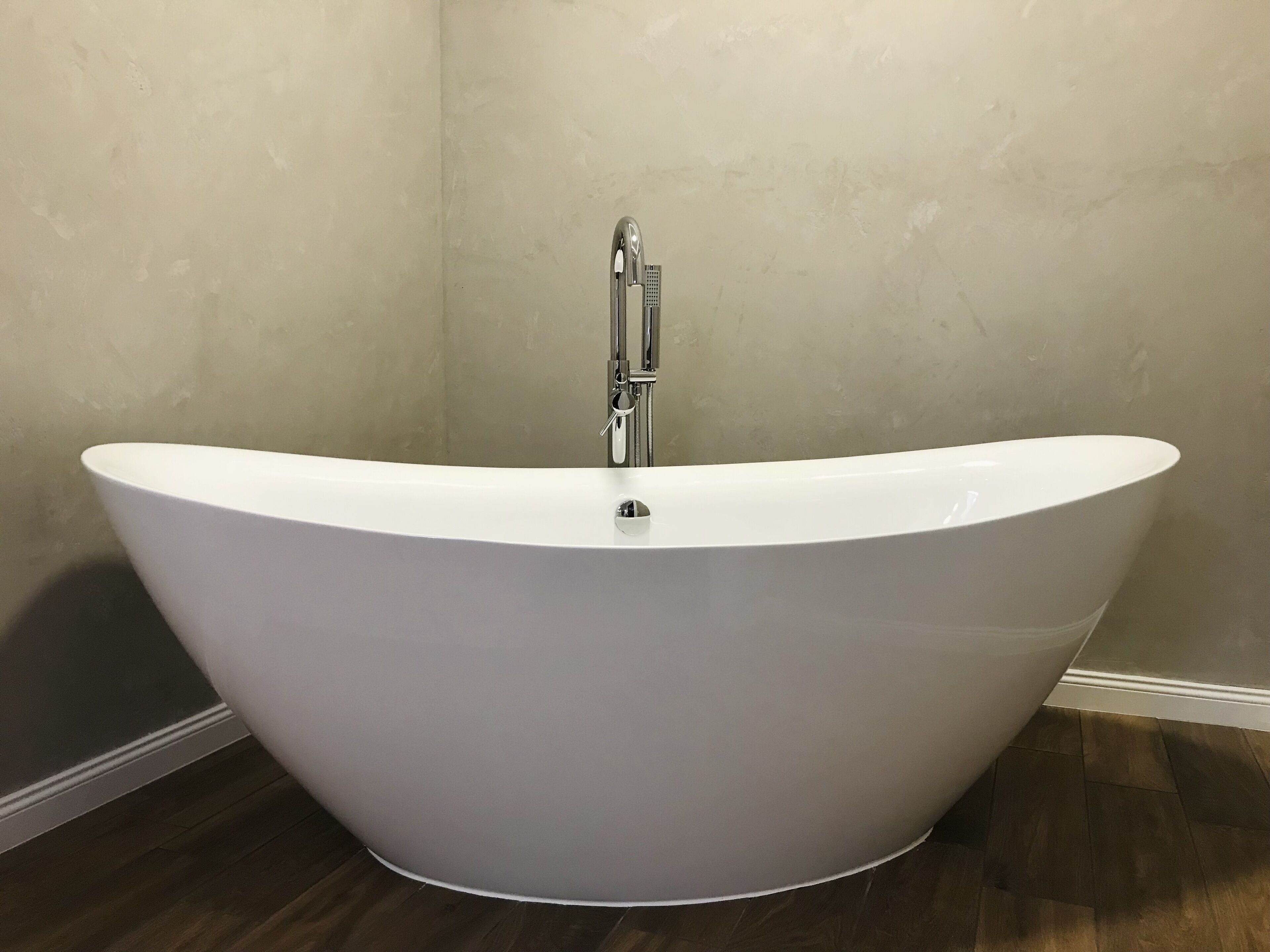 A freestanding bathtub in a bathroom with a plain wall and wooden flooring.