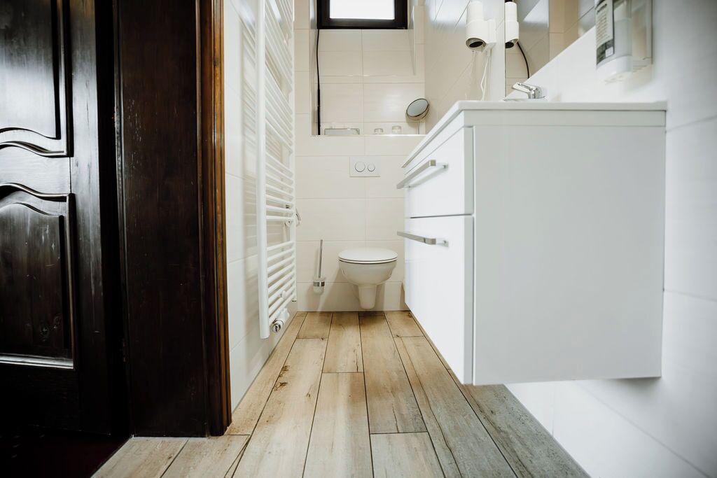 A narrow bathroom with a toilet, a white cabinet, and a wooden floor.