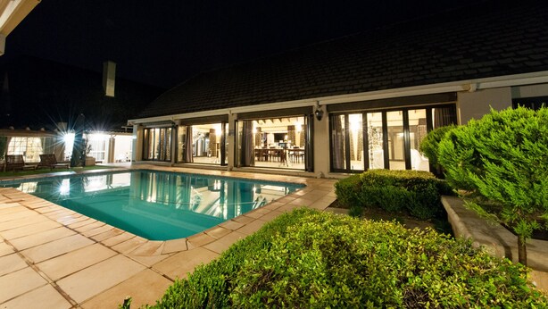 Ein Schwimmbecken mit Terrassenbereich, überdachter Sitzgelegenheit und gepflegter Bepflanzung.