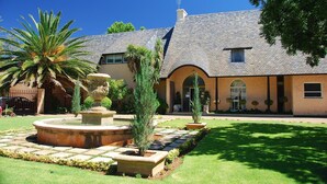 A building with a stone facade, a tiled roof, and a landscaped garden with a fountain and palm trees.