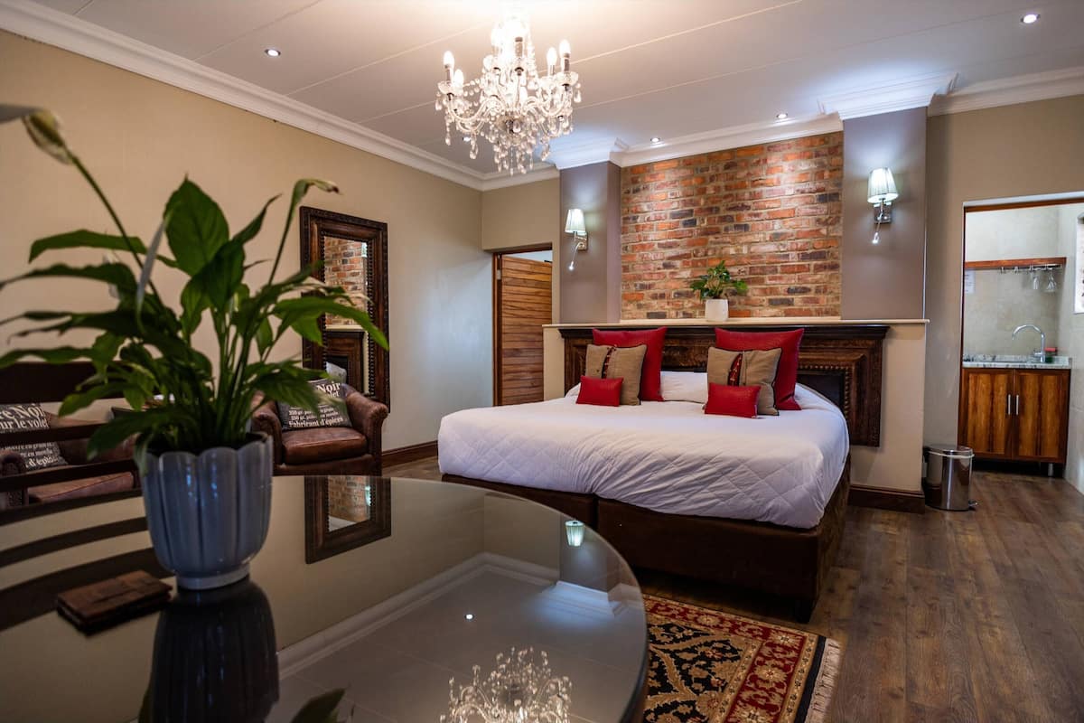 A modern bedroom with a large bed, a chandelier, a brick wall, and a small kitchen area.