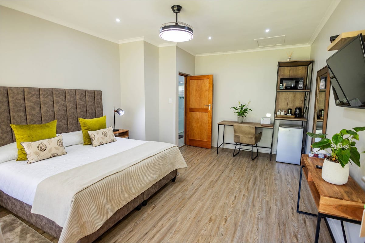 A hotel room with a large bed, a desk, a small kitchenette, and a TV mounted on the wall.