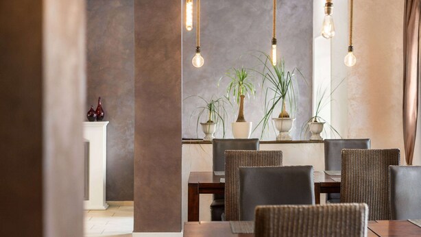 Un comedor con una mesa y sillas de madera, plantas en macetas y lámparas colgantes.