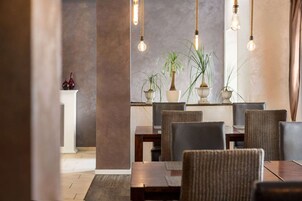 Un comedor con una mesa y sillas de madera, plantas en macetas y lámparas colgantes.