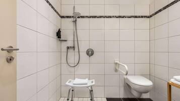A small, modern bathroom with white tiles, a shower, a toilet, and a grab bar.