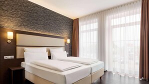 Una cama doble con cabecera, lámparas de noche, mesitas de noche y un ventanal con cortinas.