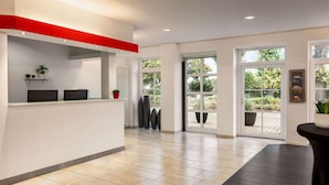 Un área de recepción moderna con un mostrador blanco, una pared de acento roja y amplios ventanales que ofrecen vistas al exterior.