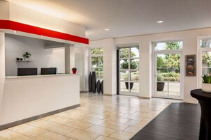 Un área de recepción moderna con un mostrador blanco, una pared de acento roja y amplios ventanales que ofrecen vistas al exterior.