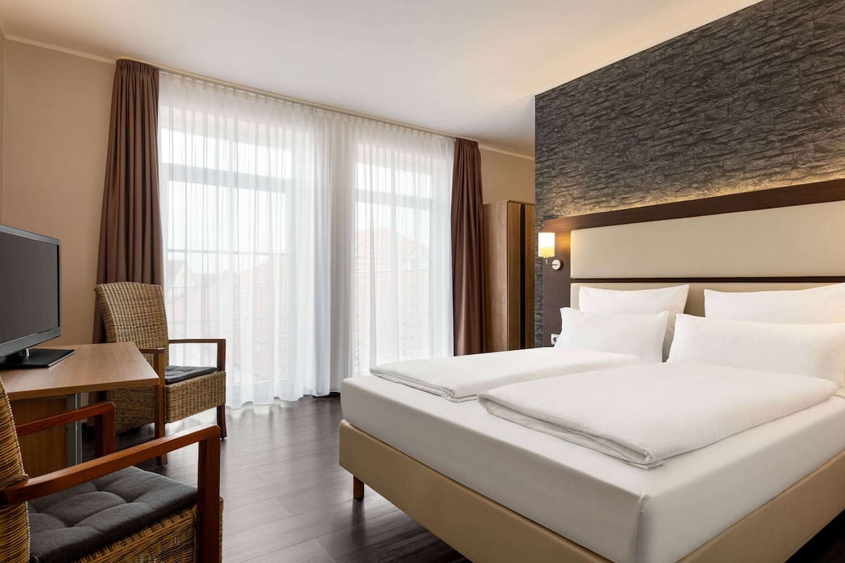 Habitación de hotel con cama, escritorio, silla y televisor.