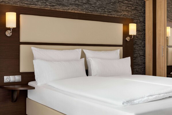 A neatly made bed with white linens, a wooden headboard, and two wall-mounted light fixtures.