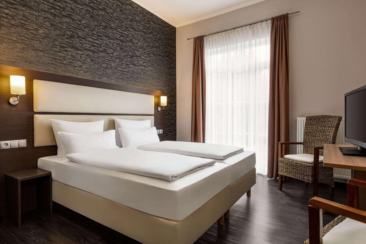 A hotel room with a large bed, a television, a chair, and a window with curtains.