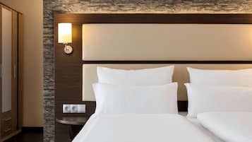 Quarto de hotel com uma cama grande, cabeceira com luminária, parede de destaque em pedra e pequena mesa de cabeceira.