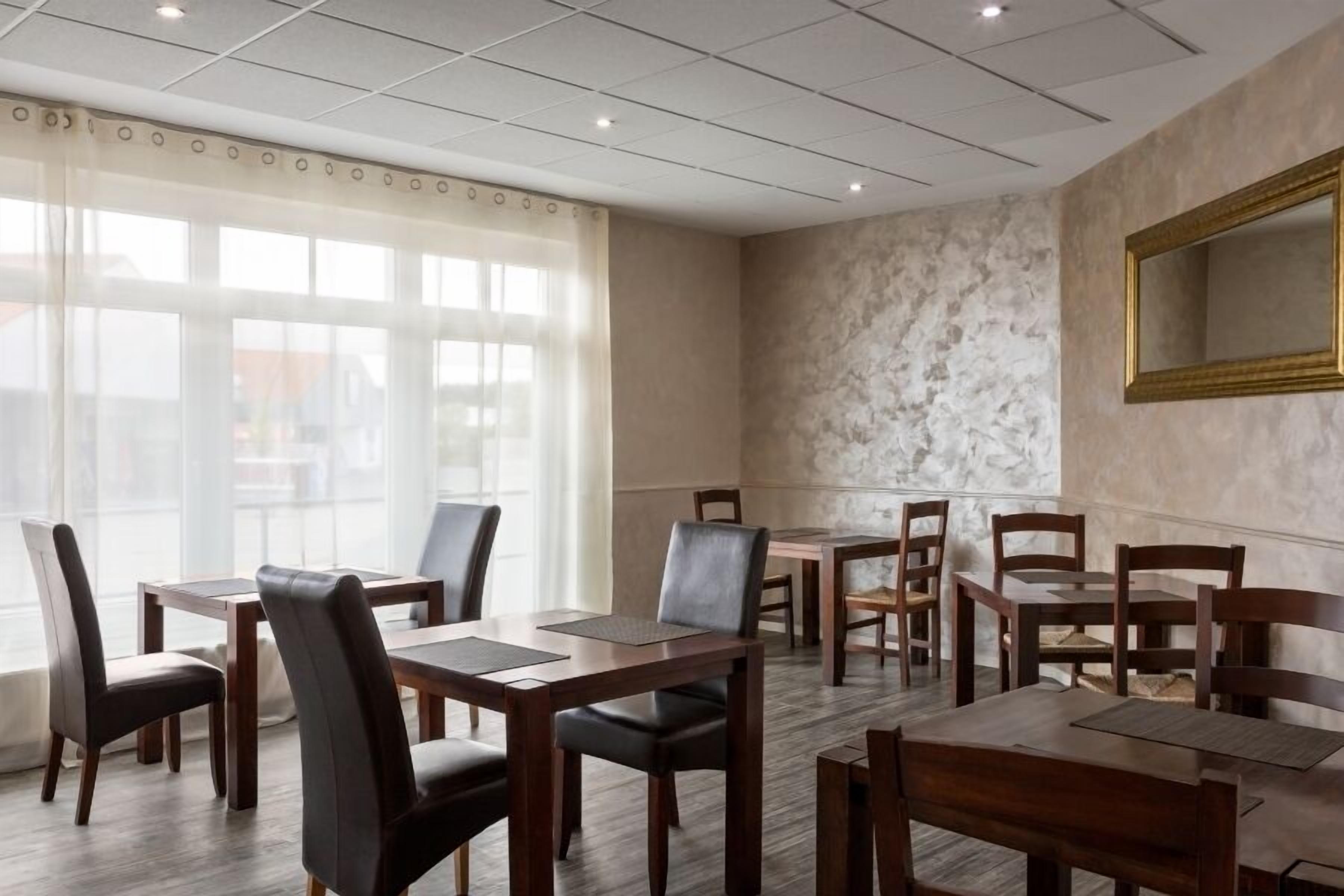 A dining area with multiple tables and chairs, large windows with curtains, and a marble wall with a framed mirror.