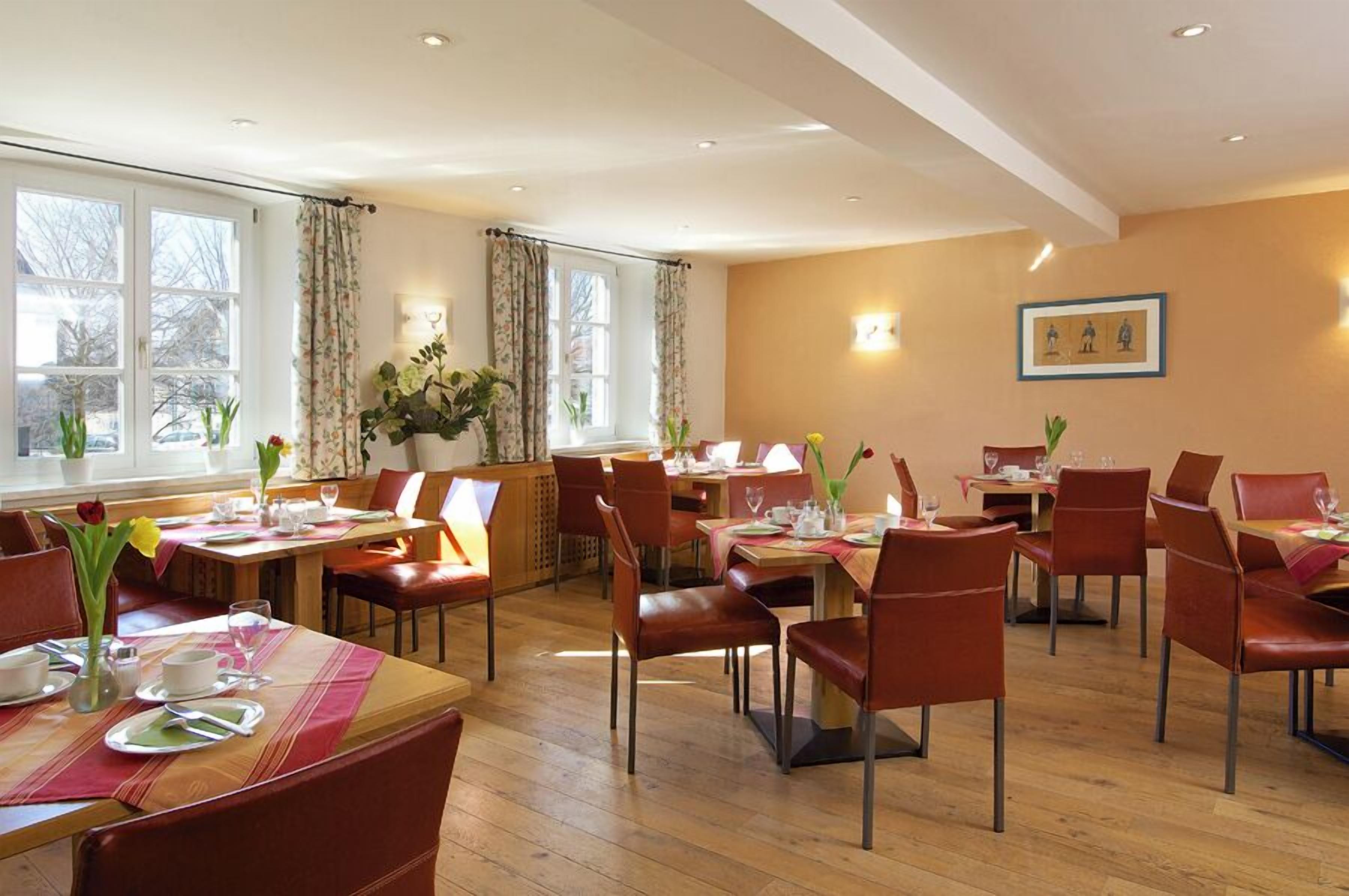 A dining area with multiple tables and chairs, large windows, and a warm interior.