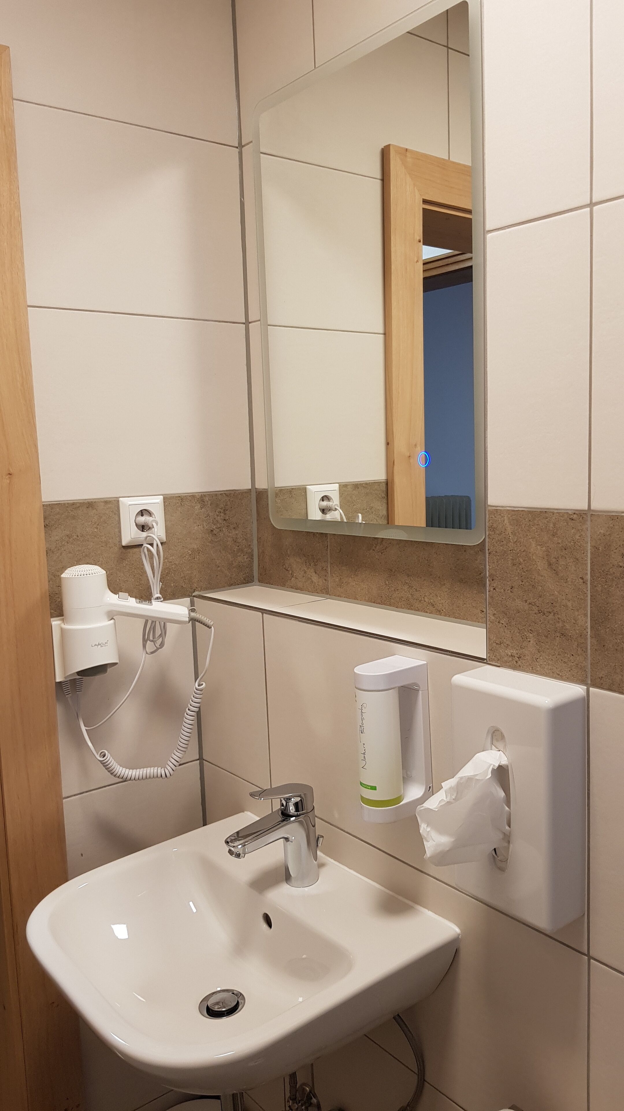 Ein Badezimmer mit Waschbecken, Spiegel, Fön und Händetrockner.