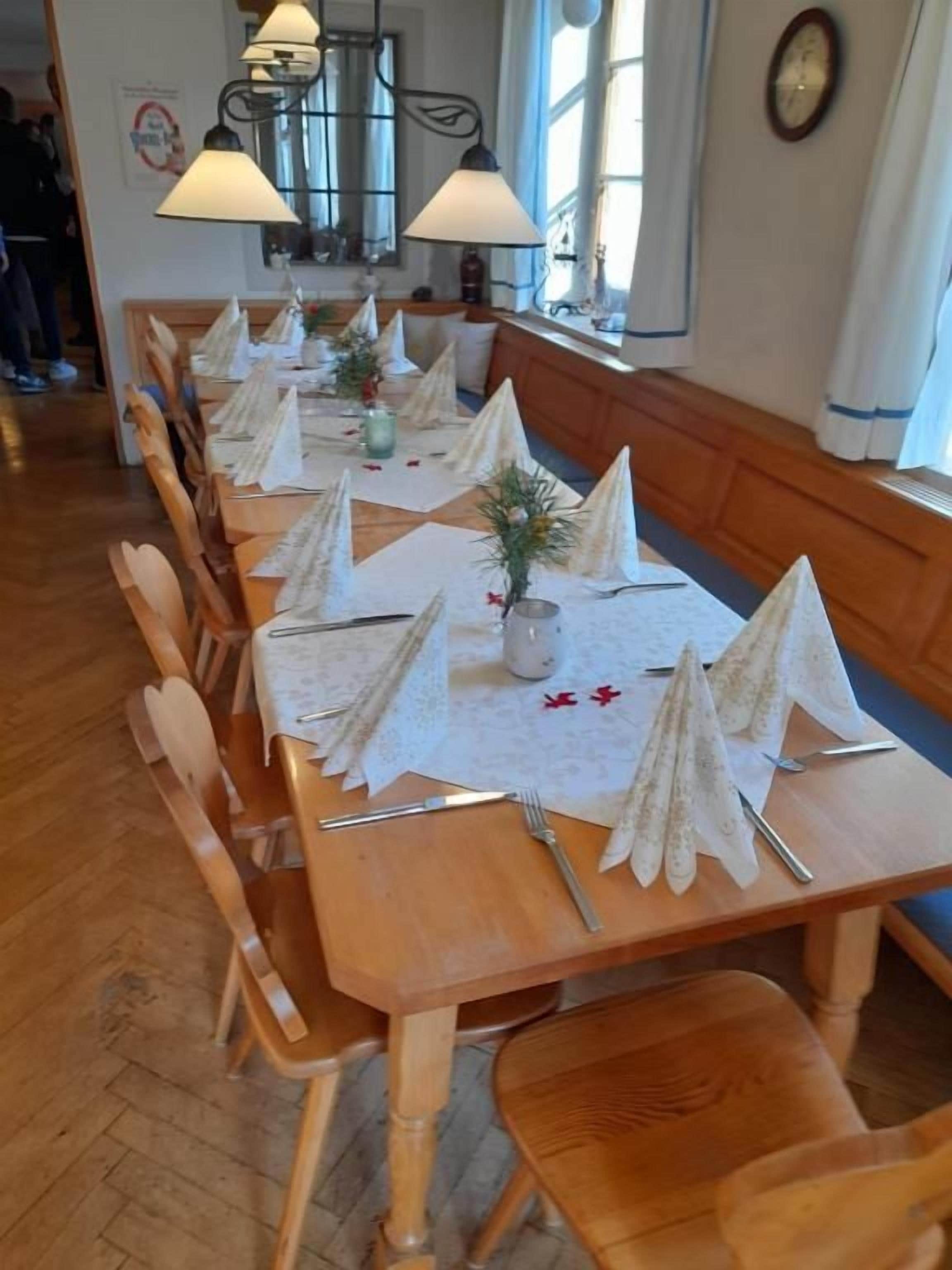 A dining area with wooden tables set with white napkins, cutlery, and small potted plants.