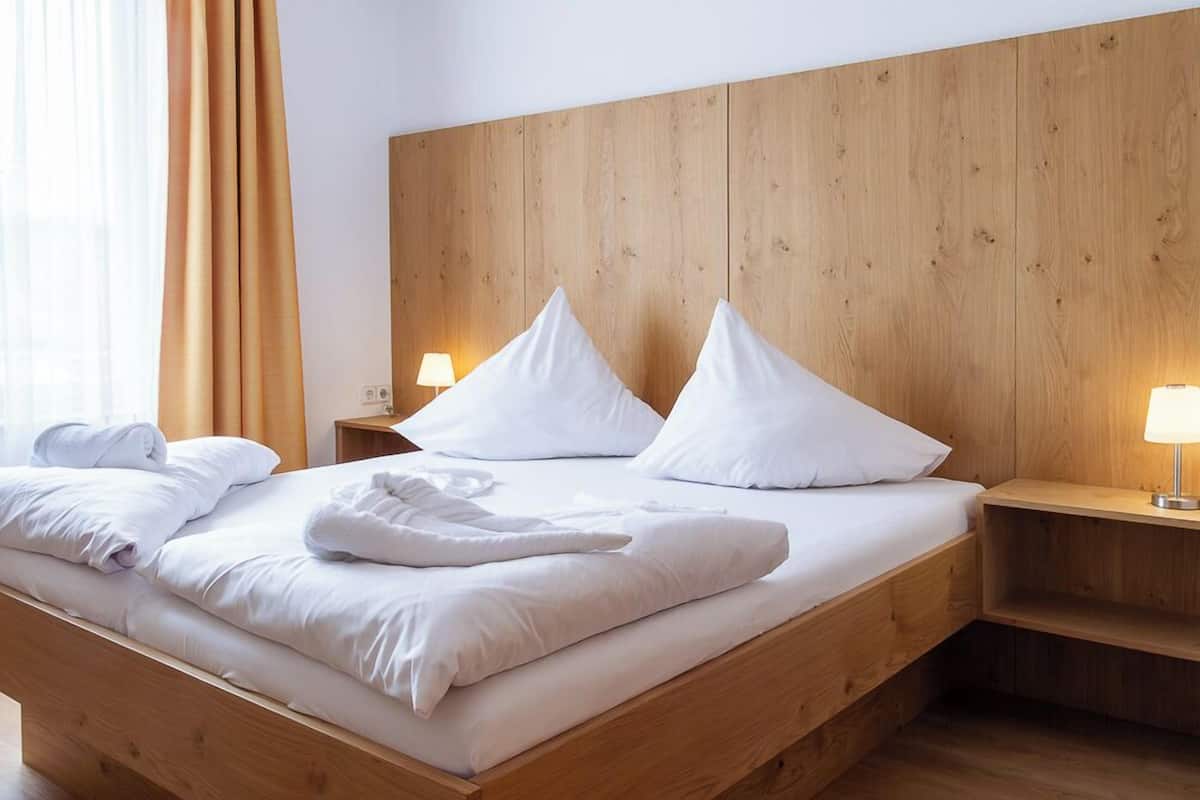 Un lit en bois avec du linge de lit blanc, deux lampes de chevet et une tête de lit en bois.