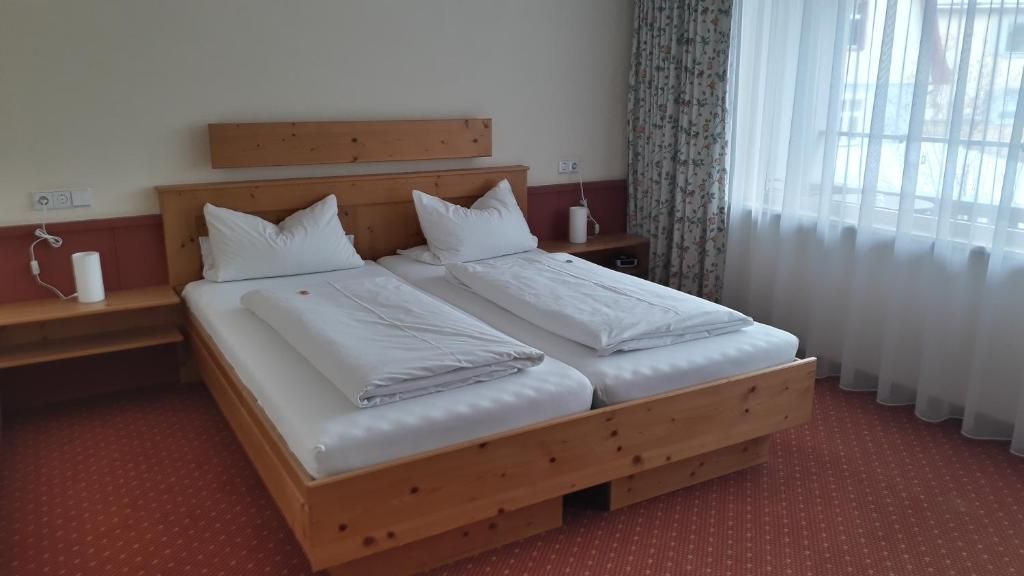 A double bed with a wooden headboard, two bedside tables, a red carpeted floor, and a window with sheer curtains.
