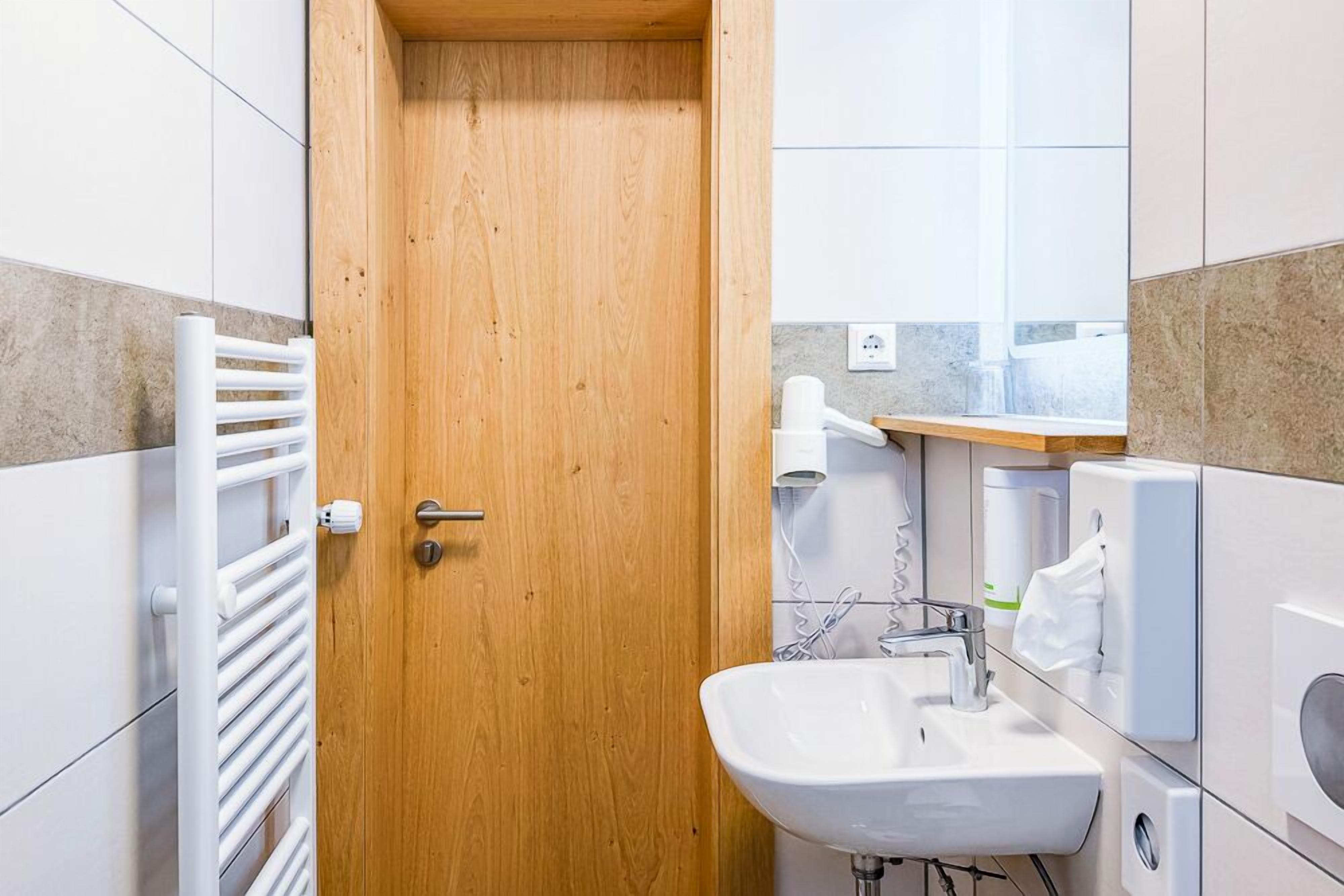 A bathroom with a wooden door, white tiles, a white sink, and a towel rack.