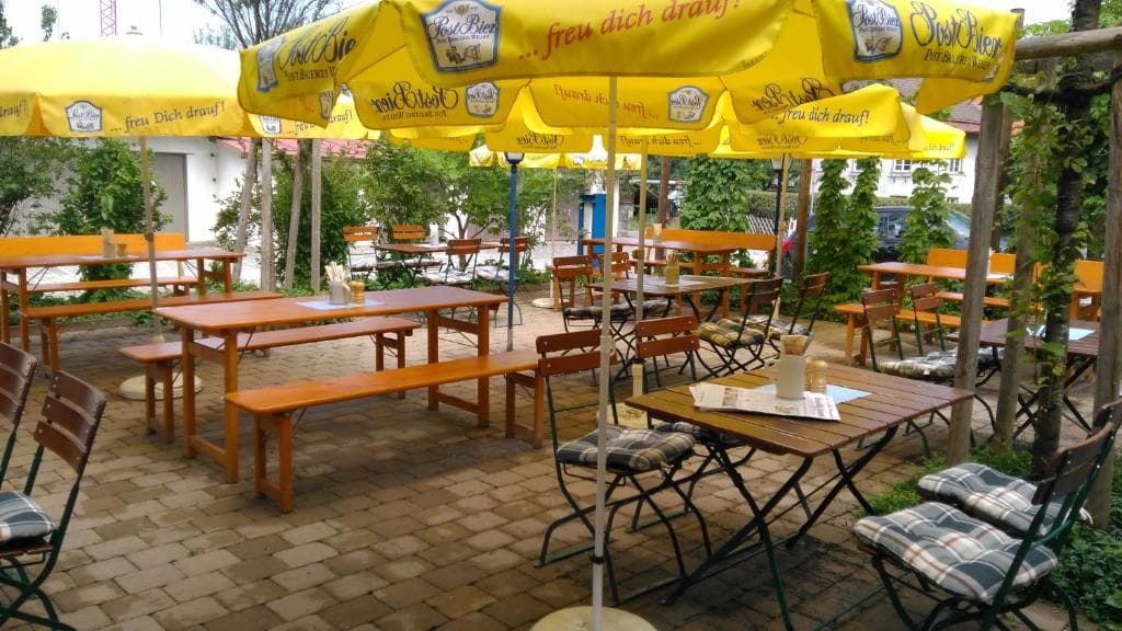 Un espace extérieur aménagé avec des tables et des bancs en bois, des parasols jaunes et un sol en briques.