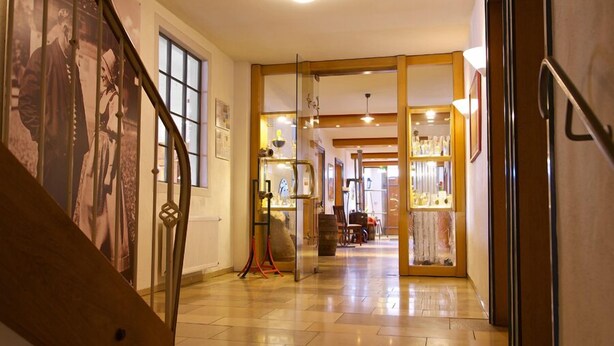 Un pasillo con una escalera, una puerta de cristal que da a una habitación con cama y cómoda, y una pared adornada con cuadros.